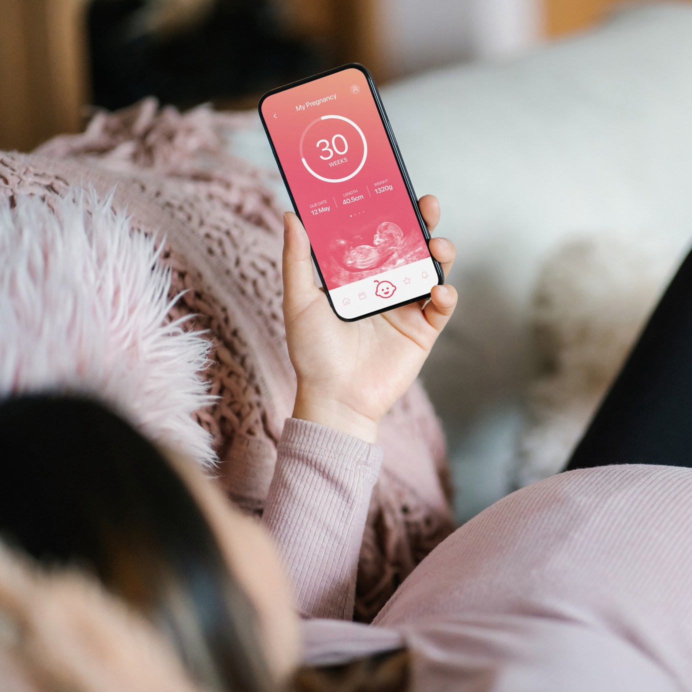 Young Asian pregnant woman lying on sofa in the living room at cozy home, using baby tracker app on smartphone to monitor her baby's growth and development throughout the pregnancy journey. Technology and pregnancy lifestyle